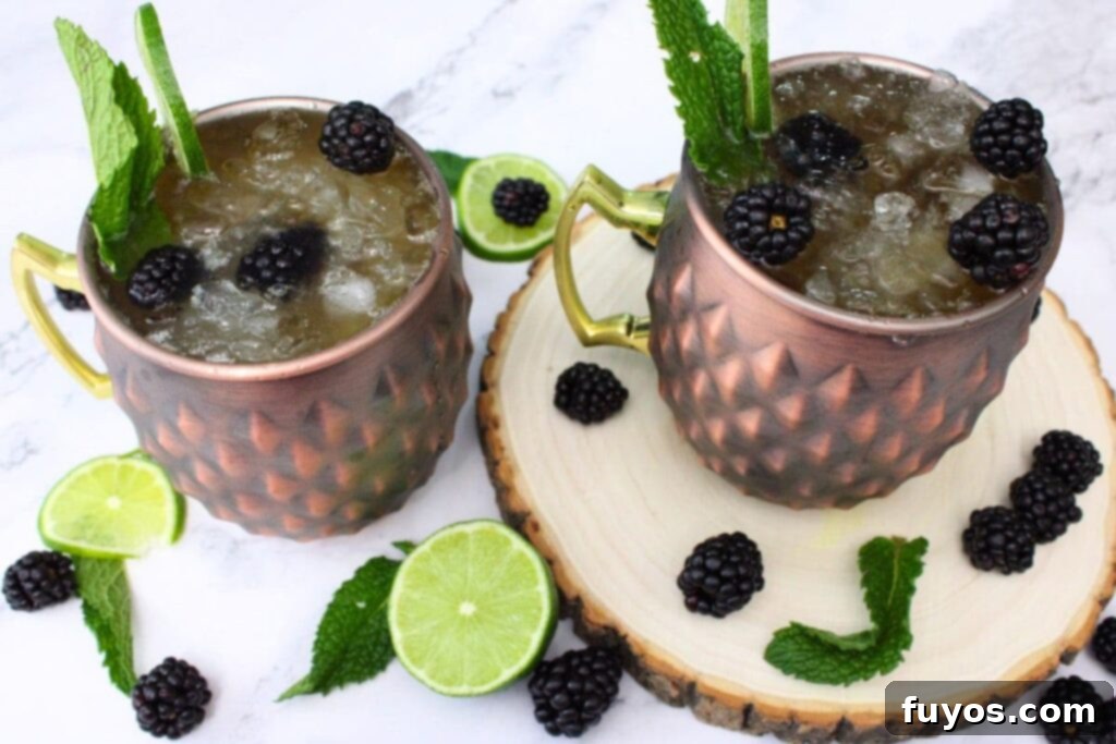 Two Blackberry Kentucky Mule cocktails, garnished with fresh lime and blackberries, with a decorative background.