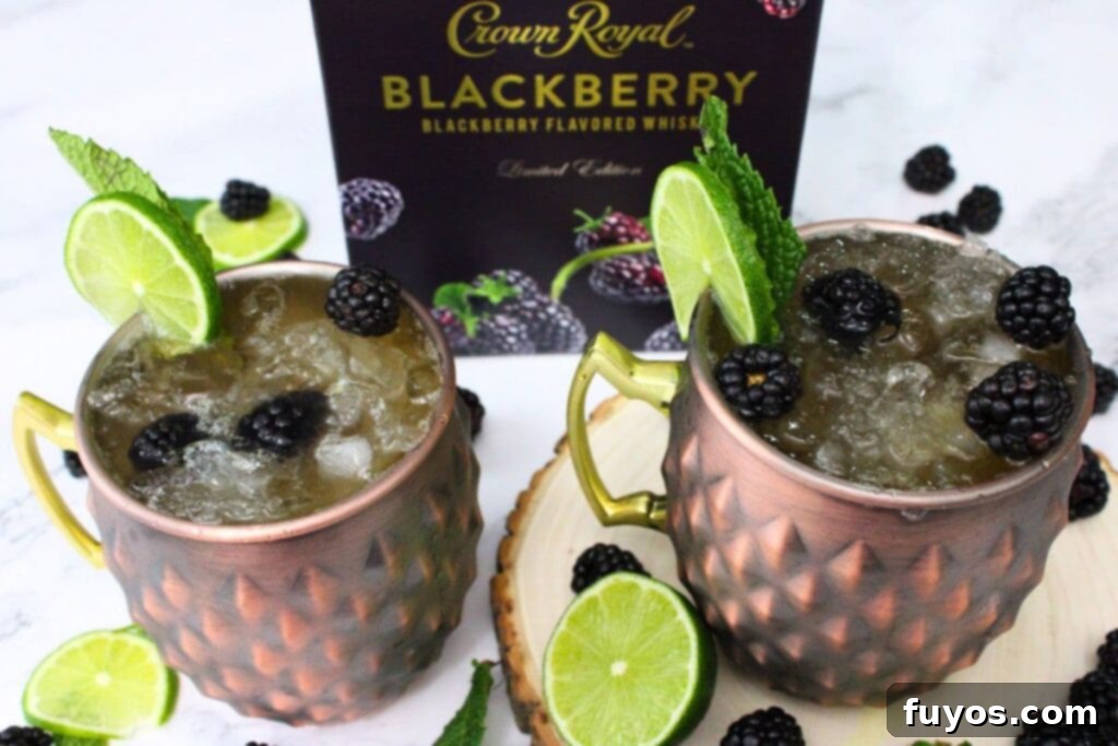 Two copper mugs filled with Blackberry Kentucky Mules, garnished with fresh berries and lime, beside a Crown Royal box.