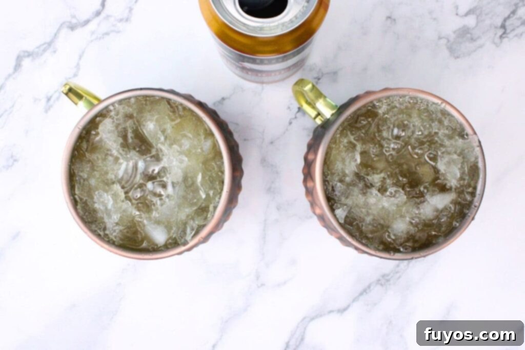 Topping a copper mug filled with blackberry whiskey and lime juice with ginger beer.