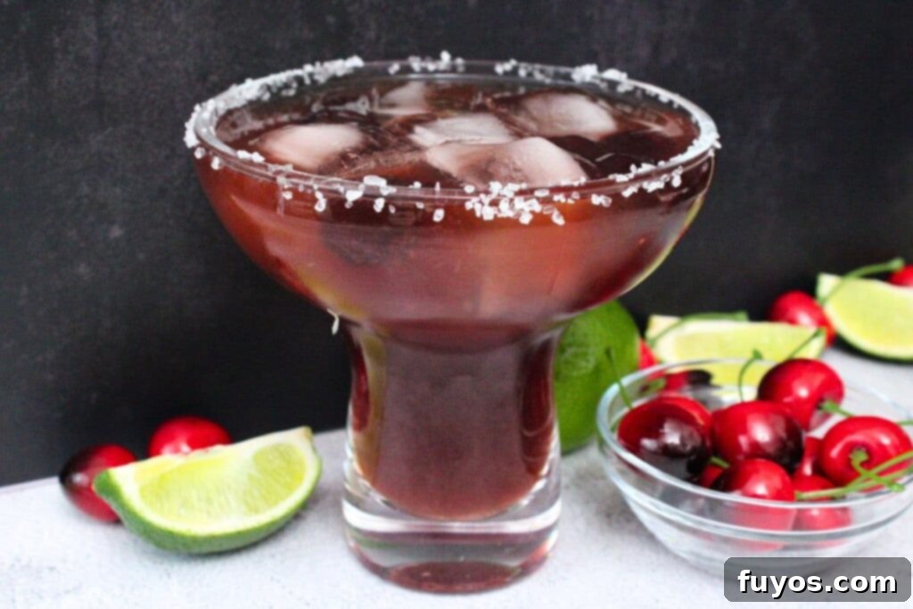 Black Cherry Tequila Burst 9 black cherry margarita against a black background with limes and cherries next to it