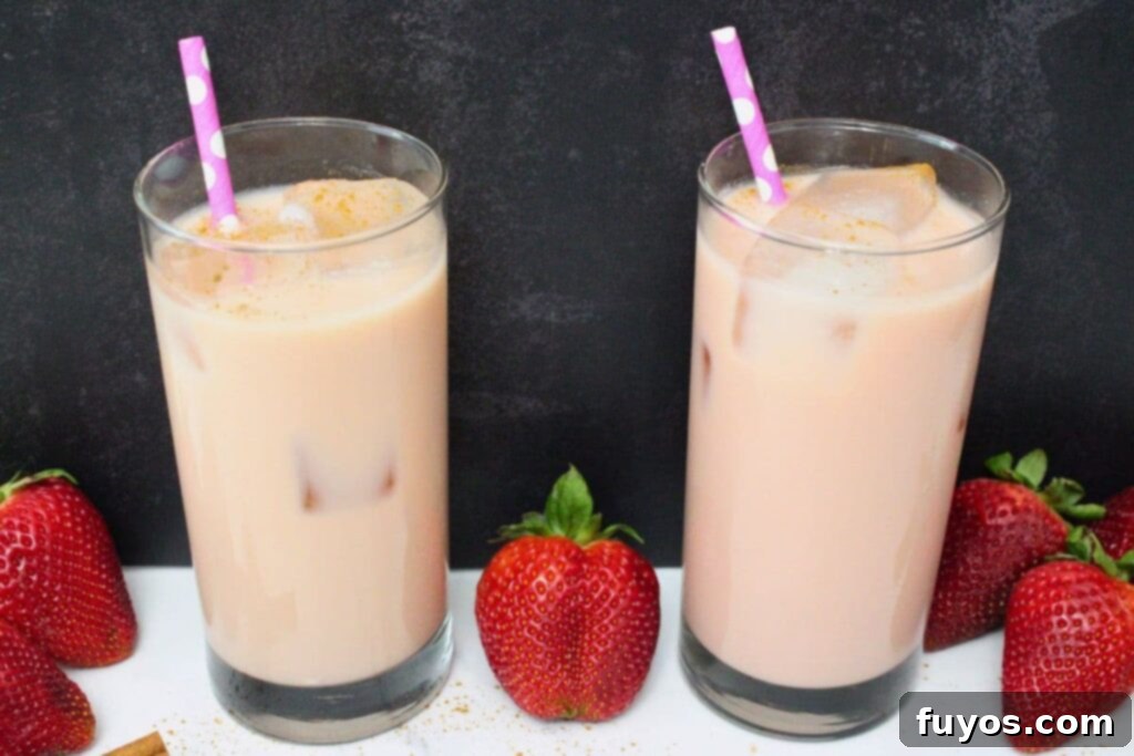 Dutch Bros Inspired Strawberry Horchata Chai 8 Two perfectly prepared strawberry horchata chai drinks set against a dark, moody background, adorned with fresh fruit, creating a visually appealing scene.