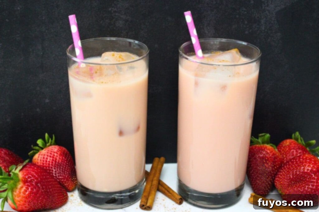 Dutch Bros Inspired Strawberry Horchata Chai 3 Two glasses of homemade Dutch Bros Strawberry Horchata Chai, artfully arranged with fresh strawberries and cinnamon sticks, highlighting its refreshing appeal.