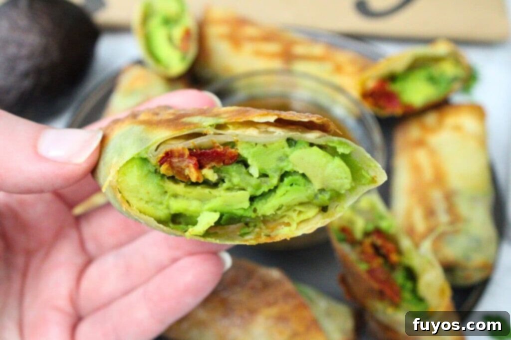 Air Fryer Copycat Cheesecake Factory Avocado Egg Rolls 3 holding up a cut in half air fryer avocado egg roll showcasing the creamy filling