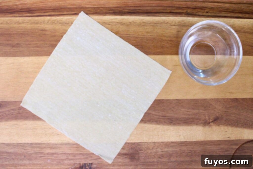 lay egg roll wrapper and a small dish of water on a cutting board