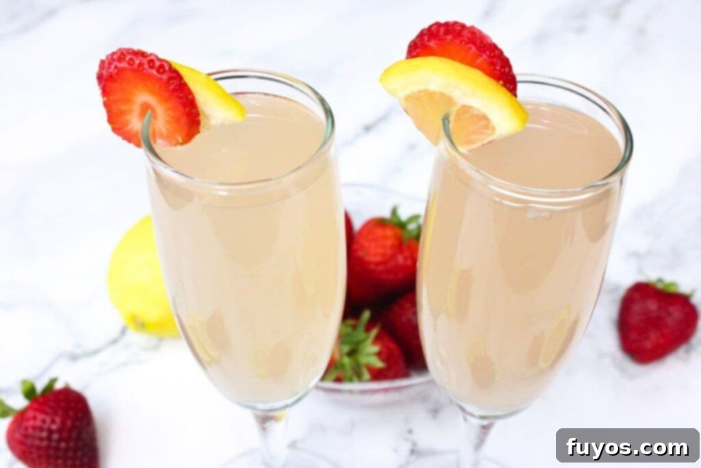 Pink Whitney Infused Strawberry Pink Lemonade Mimosa 3 Close-up of two elegant champagne flutes filled with strawberry pink lemonade mimosas, showcasing their vibrant pink color and delicate bubbles, on a pristine white marble countertop.