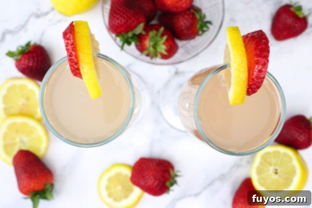 Pink Whitney Infused Strawberry Pink Lemonade Mimosa 7 Overhead shot of two perfectly garnished pink lemonade mimosa cocktails in flutes, with fresh berries and lemon slices on the rim, inviting to be enjoyed.