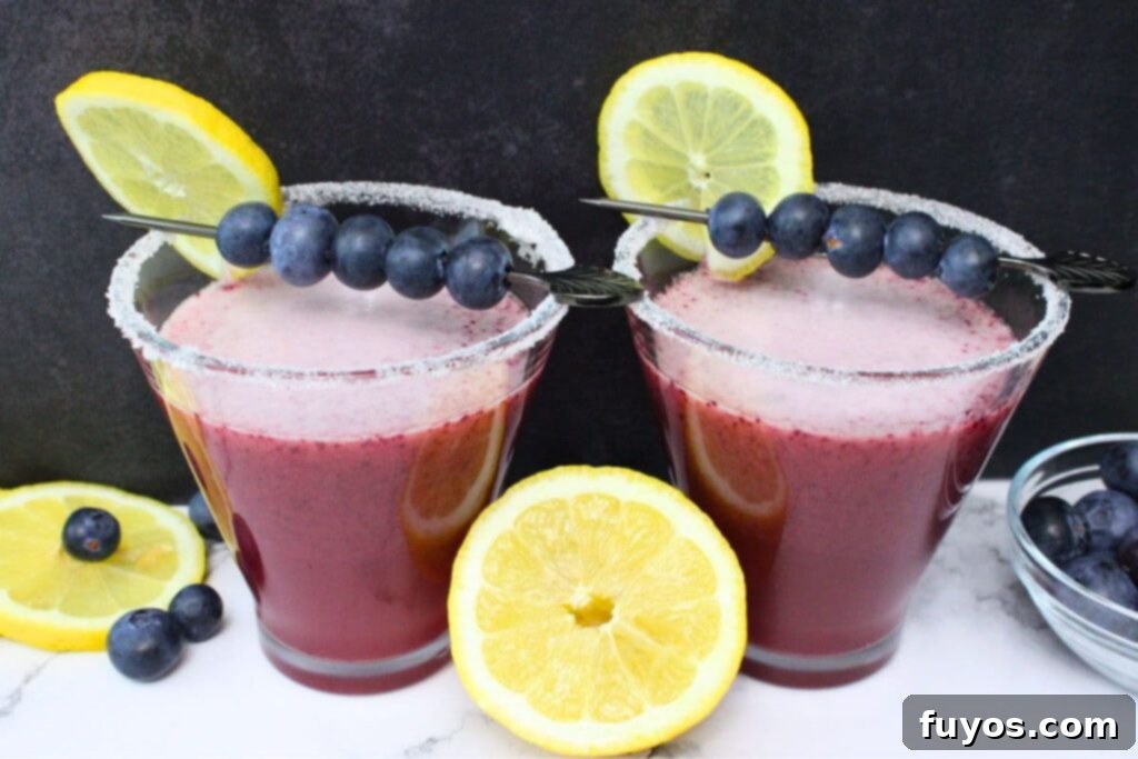 Two elegantly presented blueberry lemon drop martinis, surrounded by fresh fruit, creating an enticing visual.