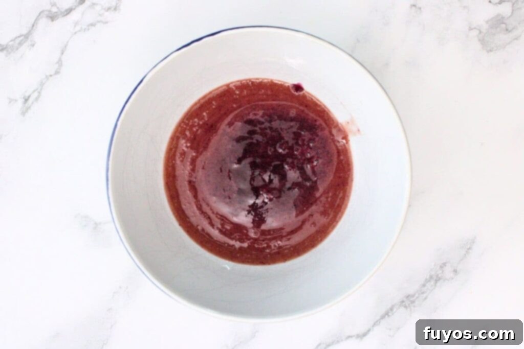 Blueberry puree being strained through a fine mesh sieve to remove any solid particles for a smoother drink.