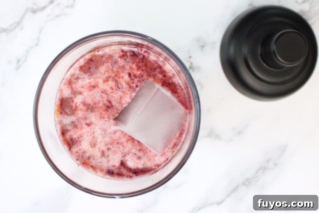 Vodka, sour mix, and blueberry puree being poured into a cocktail shaker with ice.