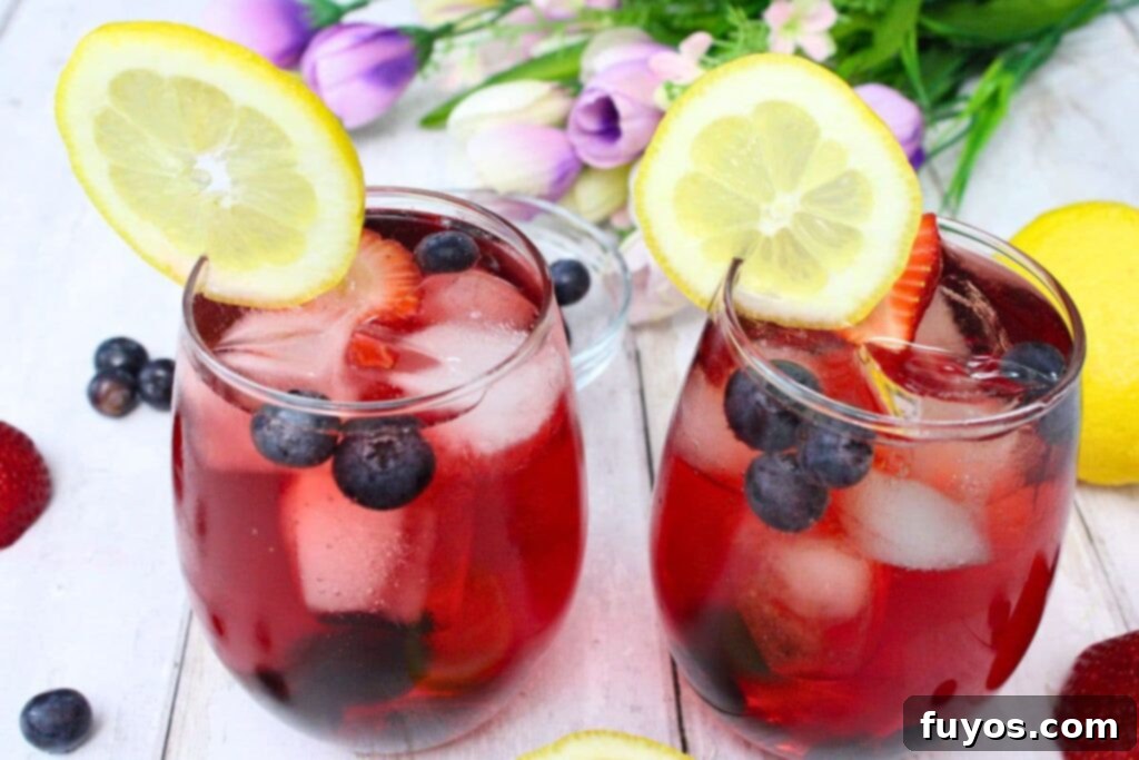 two beautiful spring spritzer cocktails with fresh fruit and lemon slices on the rim, served on a white table