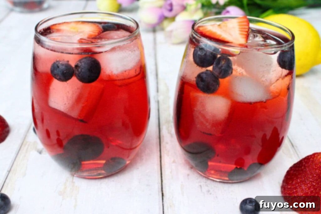 two elegant spring spritzer cocktails served in wine glasses on a rustic white wooden table, garnished with fresh berries and lemon slices