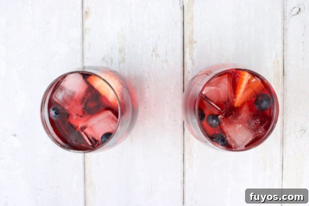 adding mixed berries and ice to the vodka aperol mixture in a wine glass