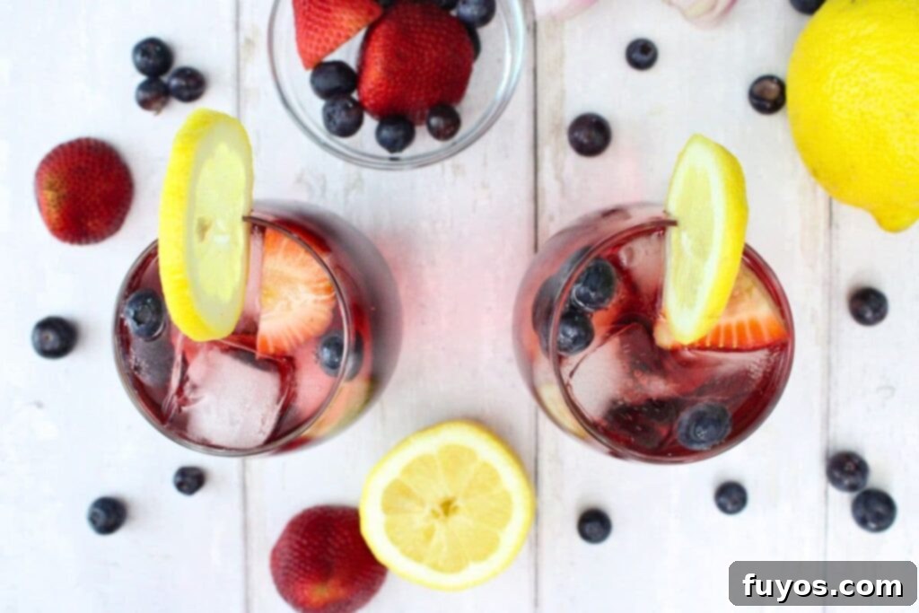 overhead view of two spring spritzer cocktails surrounded by fresh fruit on a white wooden table, garnished beautifully