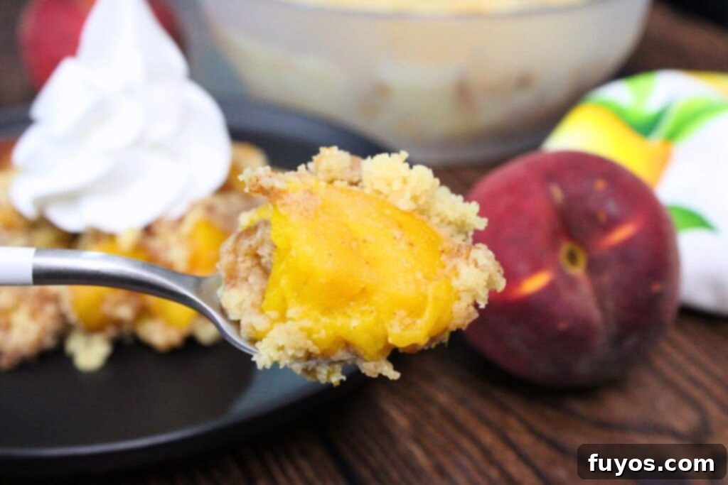 A spoonful of moist and delicious microwave peach cobbler being held up, showing the soft topping and juicy peaches.