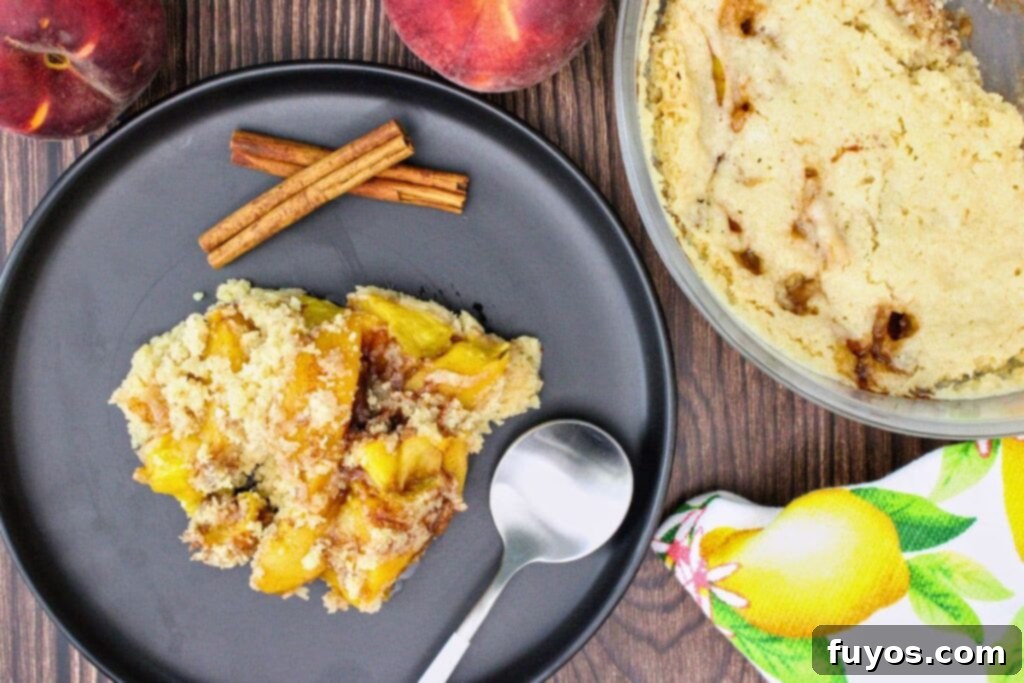 Overhead view of a warm microwave peach cobbler served on a black plate with a spoon ready to enjoy.