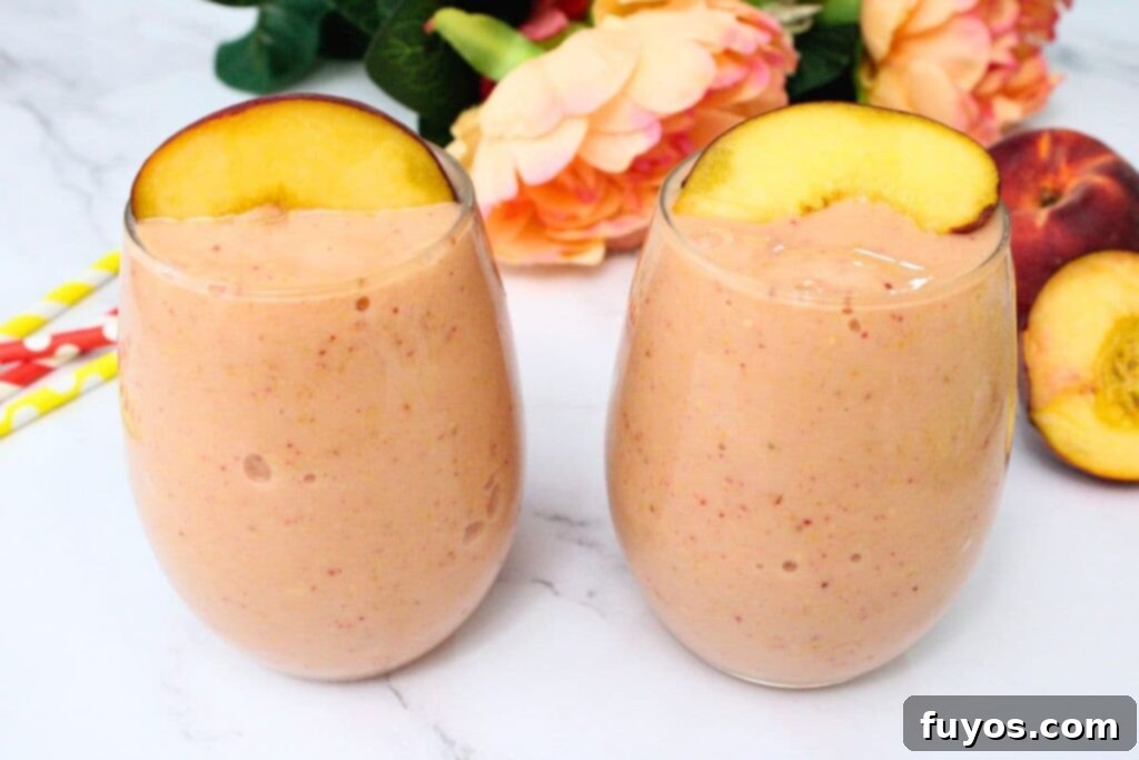 Peach Strawberry Mango Summer Bliss Smoothie 7 Two glasses of peach strawberry mango smoothie next to each other, garnished with fresh peach wedges and mint sprigs.