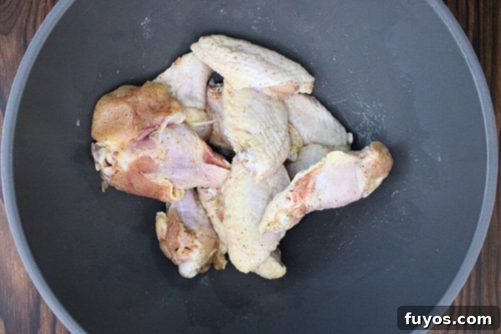 Patting chicken wings dry and coating them with olive oil and seasoning mix including salt, pepper, and baking powder