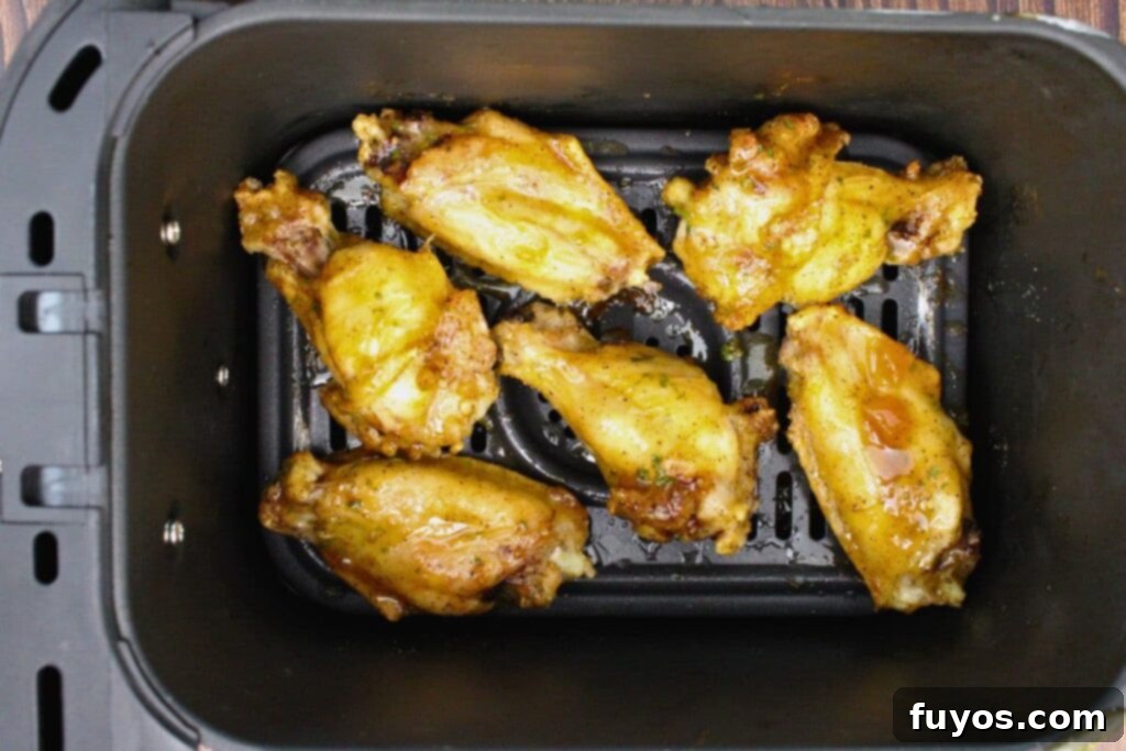 Cooked chicken wings being brushed with Crown Peach Glaze in the air fryer basket before a final cook to caramelize