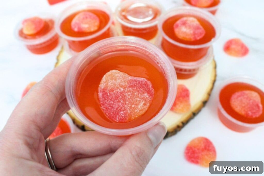 Effortless Crown Peach Jello Shots With Only Four Ingredients 3 holding up a crown peach jello shot with a candied peach on top