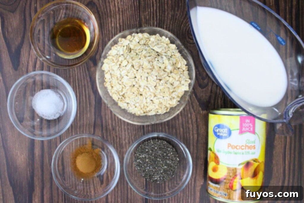 A flat lay shot showing all the ingredients for canned peach overnight oats laid out on a wooden surface: old-fashioned oats, almond milk, honey, cinnamon, salt, chia seeds, and a can of diced peaches.