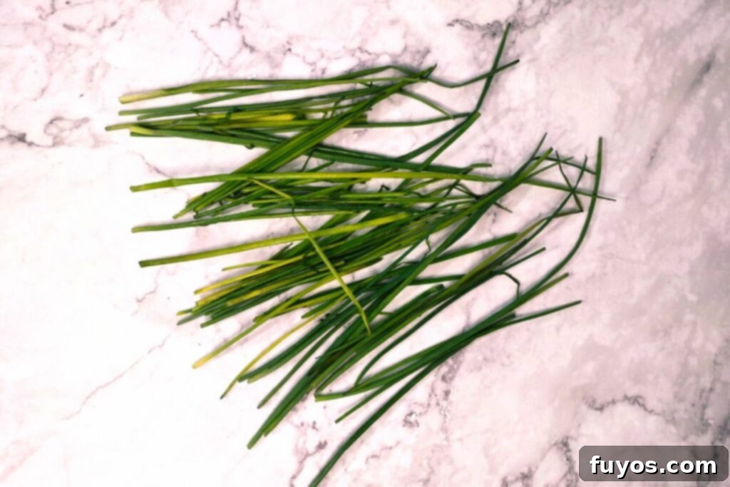 Fresh chives are laid out on a cutting board, with some visible trimming of less desirable sections before drying.