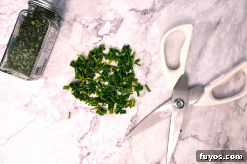 Close-up of fresh chives being cut into small pieces using kitchen shears on a cutting board.