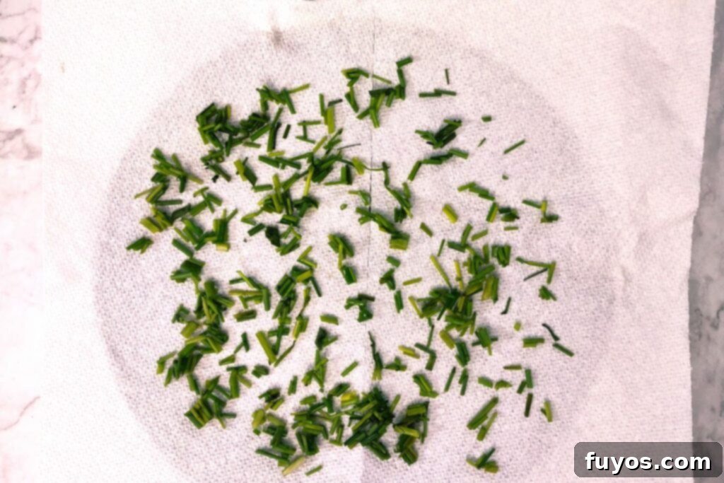 Chopped chives spread in a single layer on a paper towel laid on a microwave-safe plate.