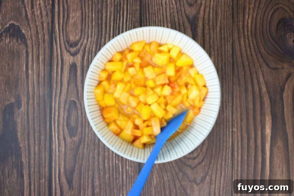 Diced peaches, cornstarch, lemon juice, Crown Royal Peach whisky, and brown sugar mixed in a small bowl, ready for cooking.