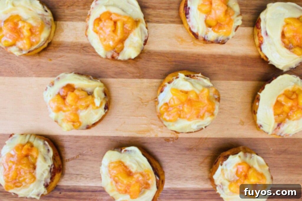 The cooled peach topping being spooned over frosted cinnamon rolls.
