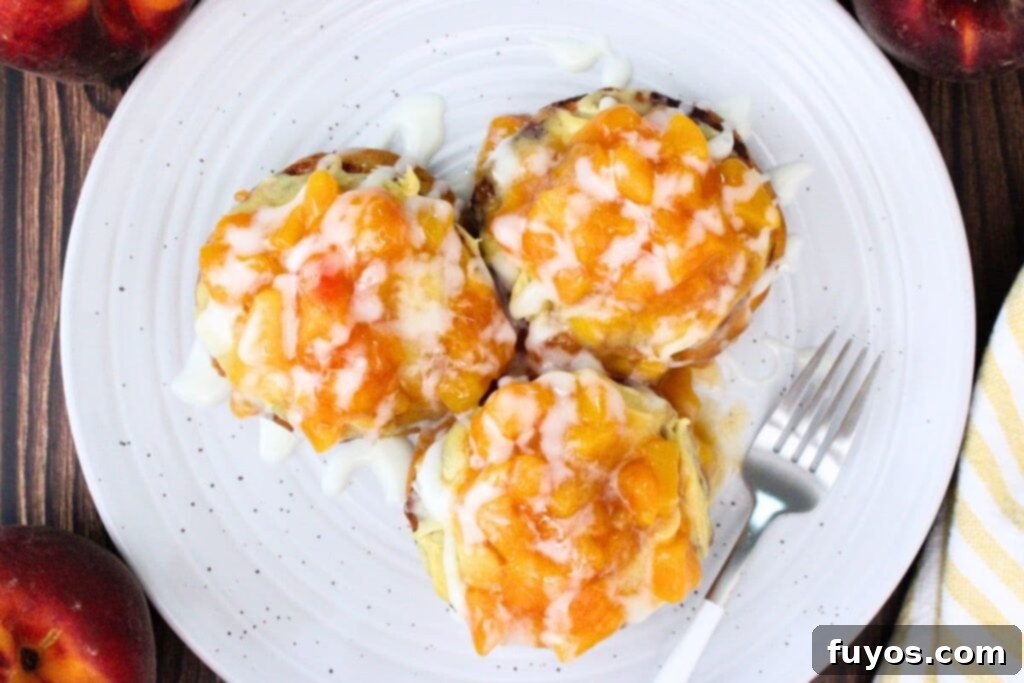 Overhead view of three finished Crown Royal peach cinnamon rolls on a white plate with a fork, showing the peach topping and melted glaze.
