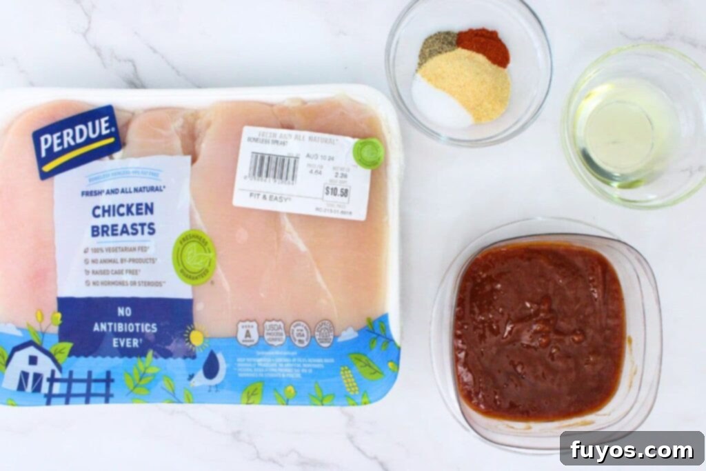 Simple Air Fryer Peach Whiskey BBQ Chicken Recipe 4 A flat lay of fresh ingredients to make peach whiskey BBQ chicken in the air fryer, including chicken breasts, spices, olive oil, and a bottle of peach whiskey BBQ sauce.