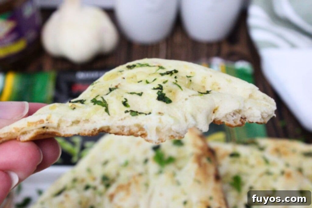 A hand holding a piece of air-fried Trader Joe's garlic naan, showcasing its fluffy texture and garlic bits.