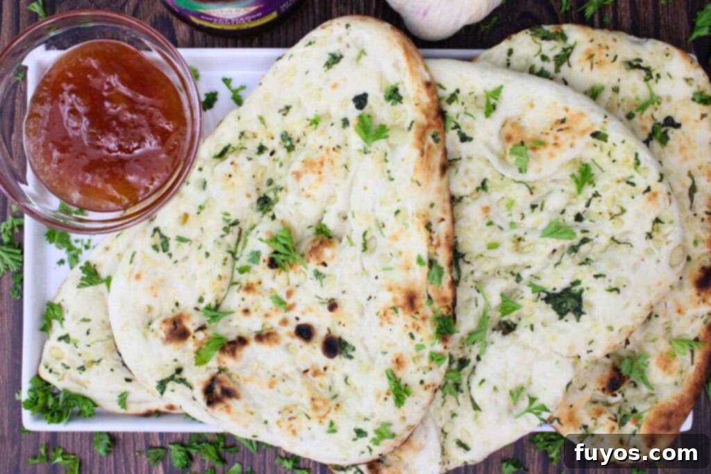 Overhead view of several pieces of golden-brown Trader Joe's garlic naan on a platter, accompanied by a small bowl of mango chutney.