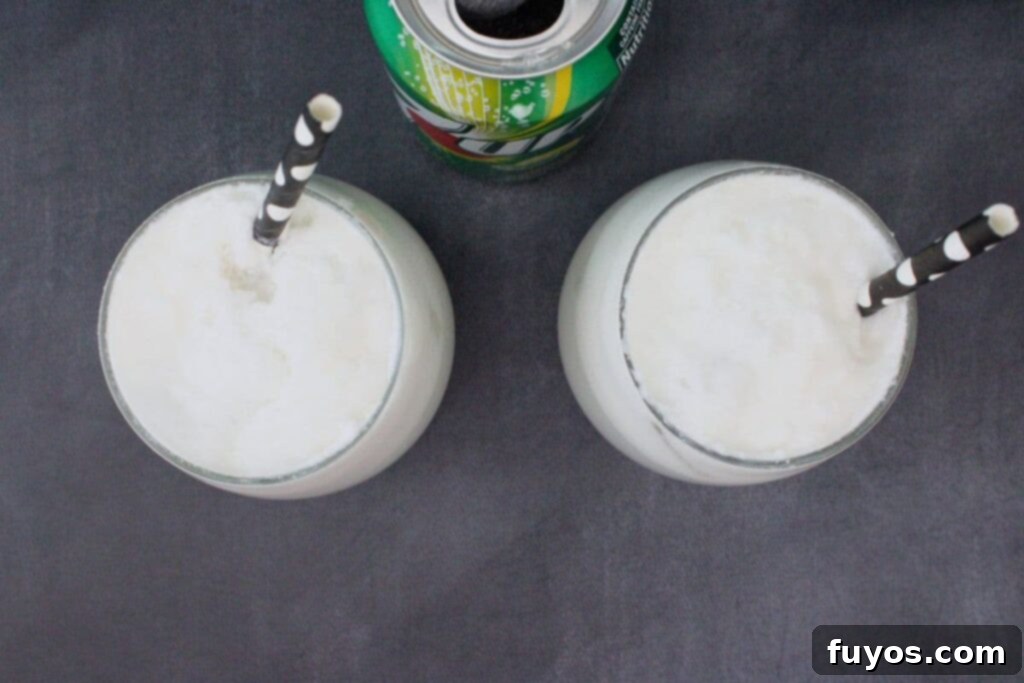 A hand pouring Sprite or 7-Up into a glass already filled with ice and the creamy Drunk Ghost Cocktail mixture, showing the final step before garnishing.