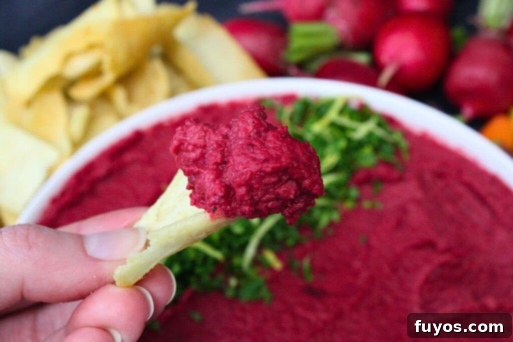 Air Fryer Roasted Beet Hummus 3 holding up a pita chip dipped in air fryer roasted beet hummus
