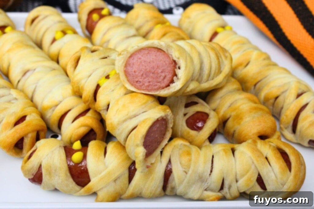 Air Fryer Mummy Dogs Your Easy Halloween Fun 3 air fryer mummy hot dogs stacked on a plate with one cut in half