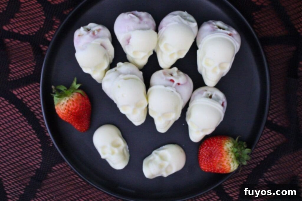 overhead view of several white chocolate strawberry skulls on a black plate