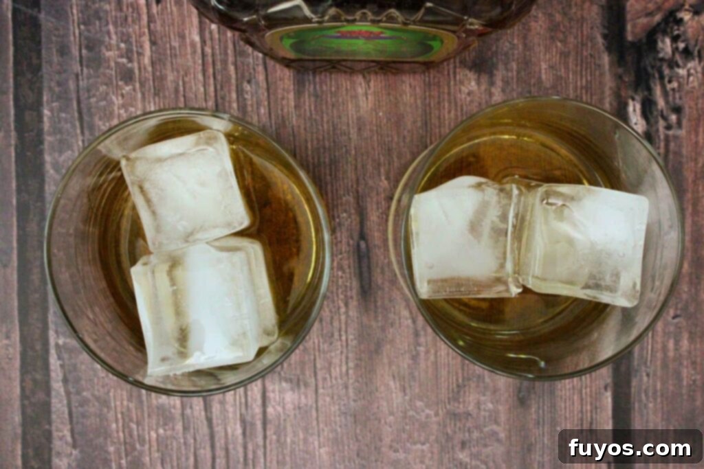 Crownberry Apple Two Ingredient Autumn Delight 6 A hand pouring Crown Royal Apple whiskey into a lowball glass filled with ice, a key step in making the Crownberry Apple.