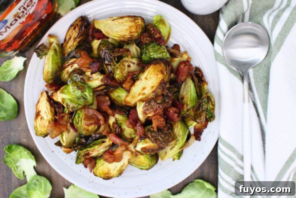 overhead view of air fryer brussel sprouts with maple syrup bacon on a plate next to a spoon and napkin
