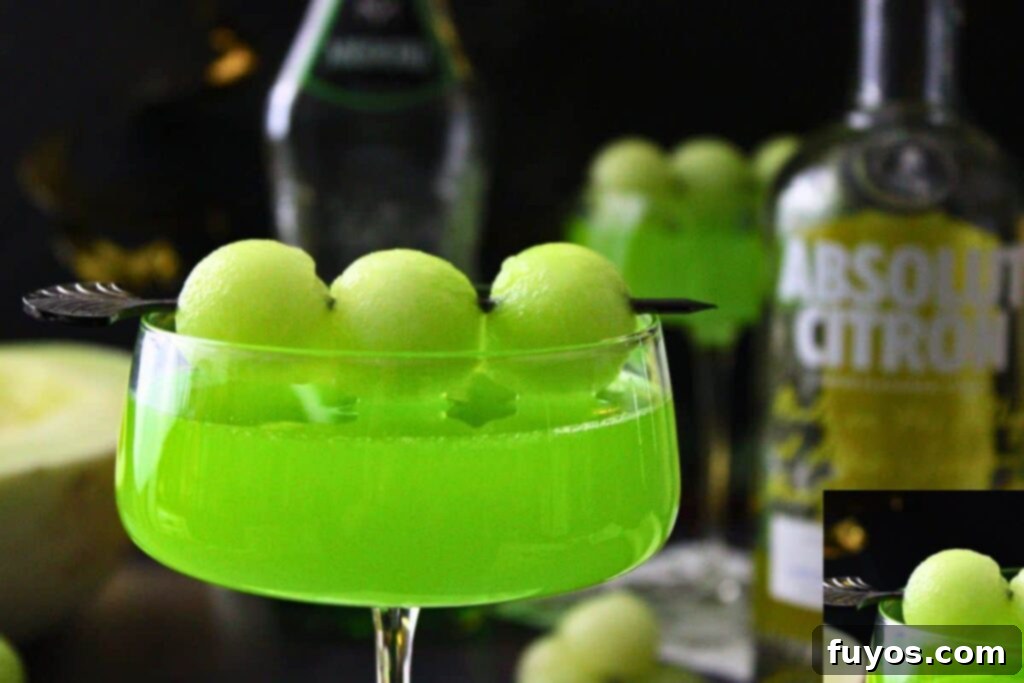 closeup of melon ball drop cocktail with melon ball skewer in front of liquor bottles
