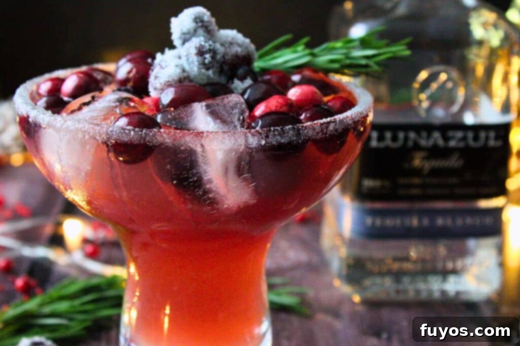 Frosted Mistletoe Margarita Christmas Cocktail 3 Festive frosted mistletoe margarita with sugared cranberries next to a tequila bottle, ready for holiday parties