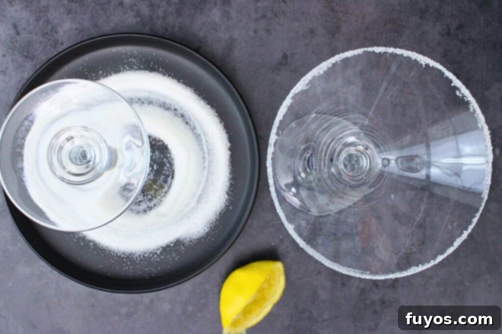 Hands rimming a martini glass with a lemon wedge and sugar for a Christmas Lemon Drop Cosmo.