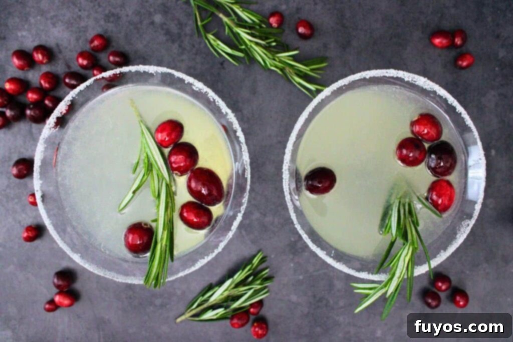 Overhead view of two Christmas Lemon Drop Cosmos in martini glasses, garnished with fresh cranberries and rosemary.