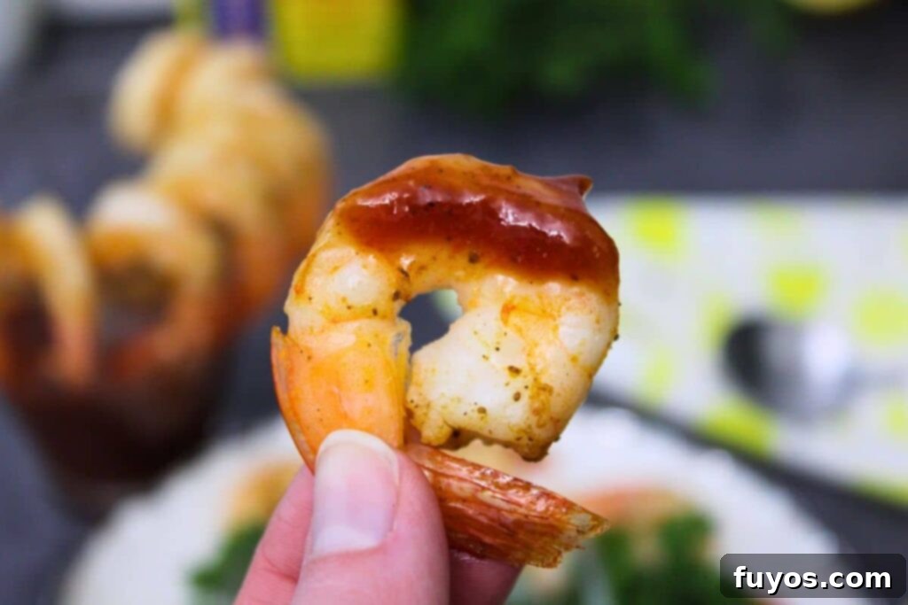 Air Fryer Shrimp Cocktail Easy Elegance 3 holding up an air fryer shrimp dipped in homemade cocktail sauce
