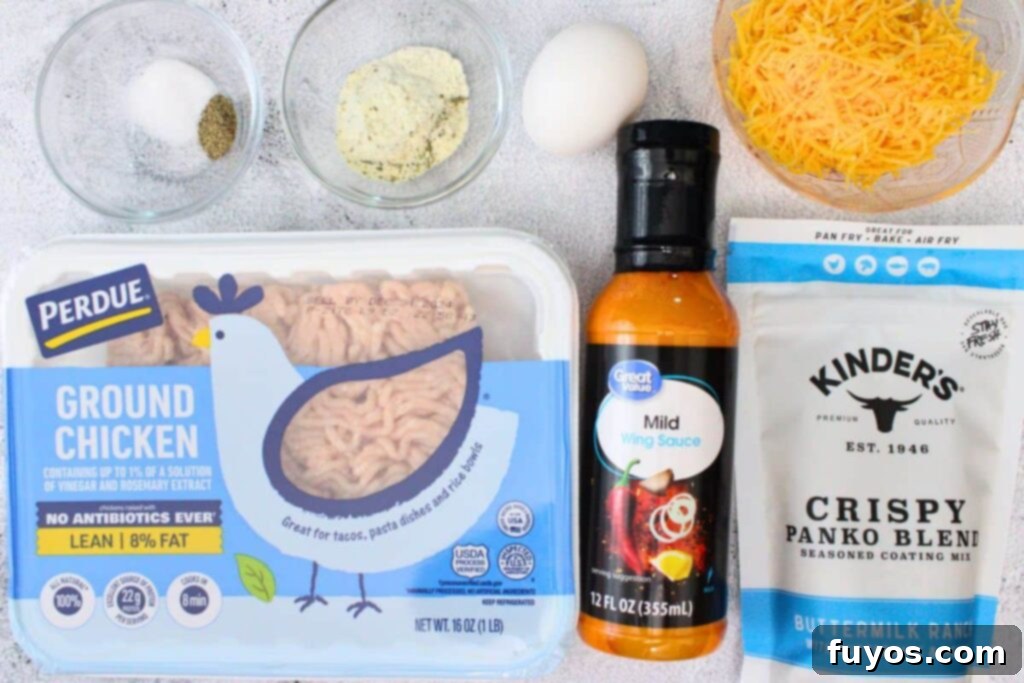 A selection of ingredients laid out, including ground chicken, panko breadcrumbs, an egg, ranch seasoning, shredded cheddar cheese, buffalo wing sauce, salt, and pepper, ready to be combined for air fryer buffalo chicken meatballs.
