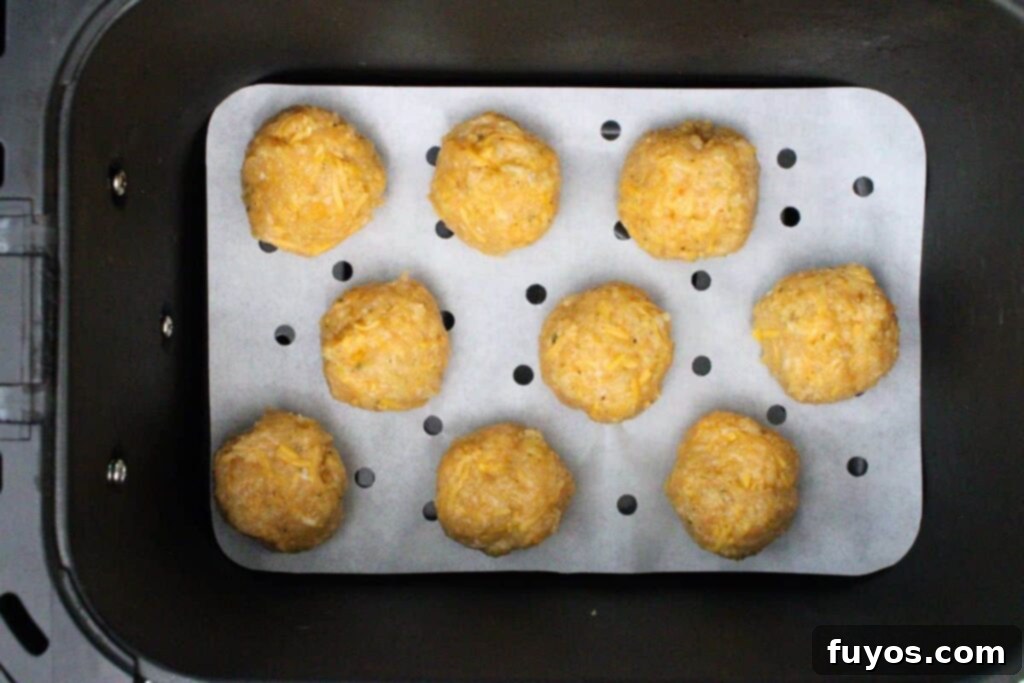 Uncooked chicken meatballs neatly arranged in a single layer within an air fryer basket, ready for cooking.