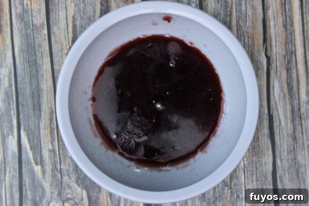 A small bowl of raspberry jam being warmed in a microwave-safe dish to achieve a runny consistency.