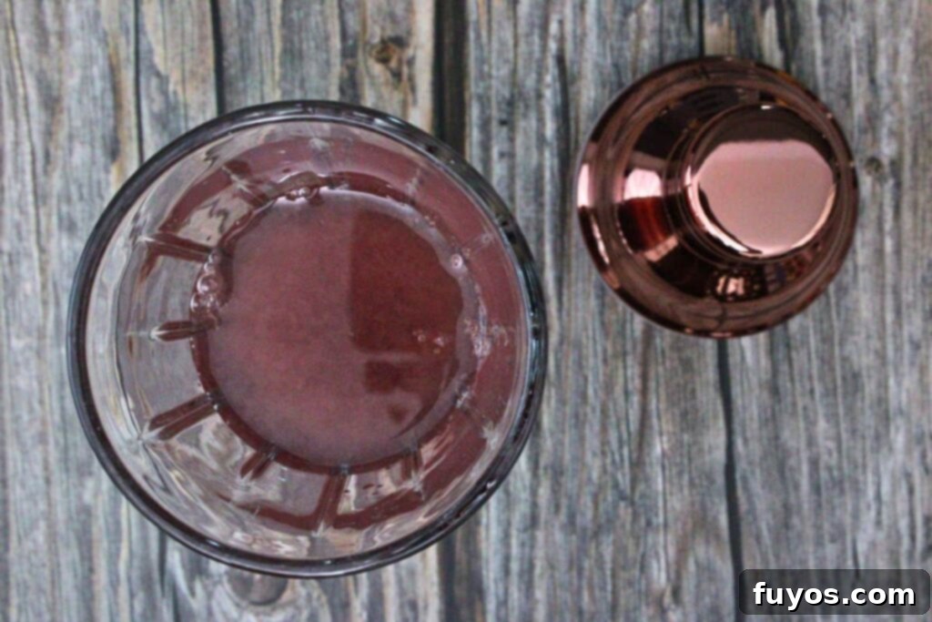 Ingredients, including warmed jam, gin, and fresh lemon juice, being added to a cocktail shaker.