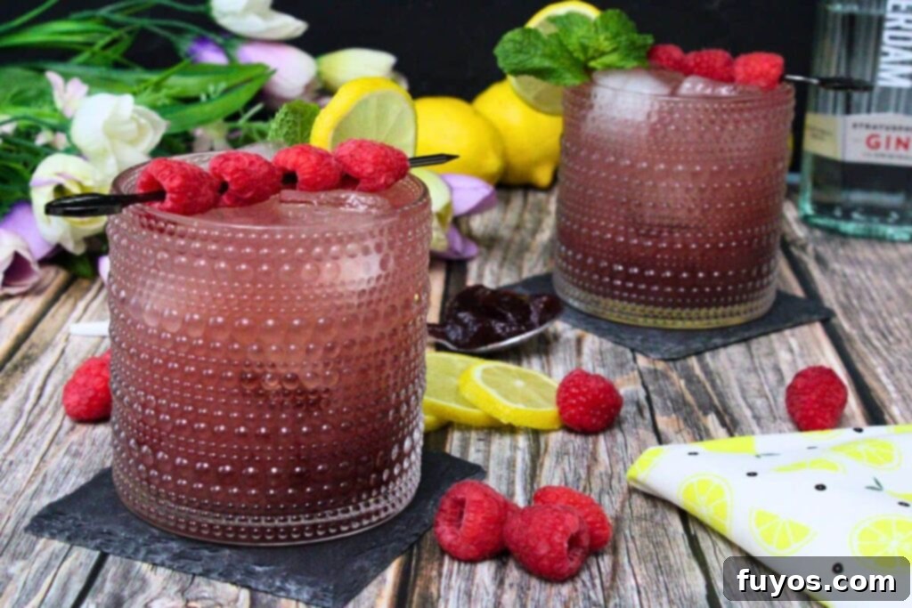 Two exquisite Gin and Jam cocktails on a wooden table, surrounded by an assortment of fresh berries, lemon slices, and delicate flowers.