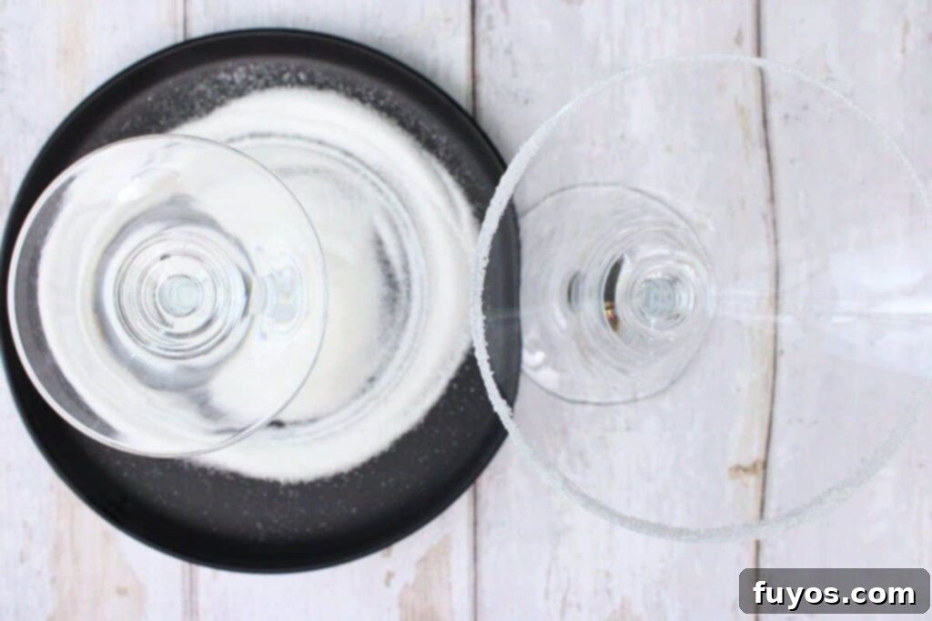 Close-up shot of a martini glass being rimmed with sugar using a lemon wedge, showing the preparation step.